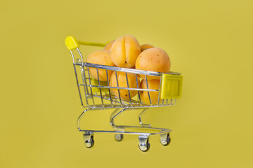 apricots in a small shopping cart on a yellow background