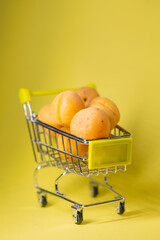 apricots in a small shopping cart on a yellow background