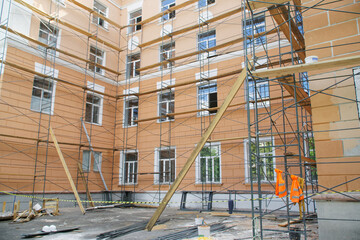 Scaffolding next to the outer wall of an urban four-story building. Capital repairs, reconstruction and restoration of city houses. Plastering and painting of external walls.