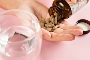 Bottle of weight loss pills and glass of water on pink background. Proper nutrition concept....