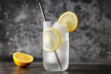 Refreshing homemade lemonade made of lemon slices, sparkling water served in glass with metal straw on  against gray wall. Image with copy space, horizontal - obrazy, fototapety, plakaty