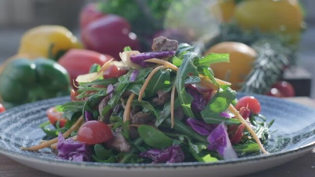Close-up of fresh salad made of red cabbige, tomatoes, onions, basil, arugula and pieces of fried meat
