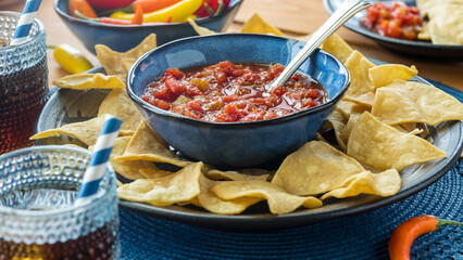 A bowl of fresh salsa nestled on a plate of crispy tortilla chips for dipping.