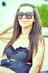 Naklejka premium Young Beautiful Happy Smiling Woman in swimsuit looking at the Phone reading a Message ,checking social media and News sitting at beach bar
