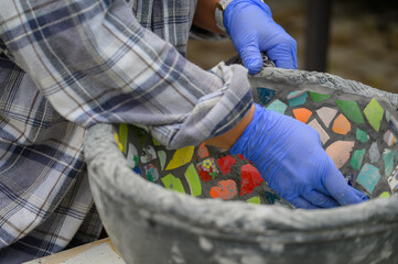People decorate earthenware with mosaic techniques in the master class or in the fresh air in the workshop. Homemade mosaic flower pot with porcelain pieces.