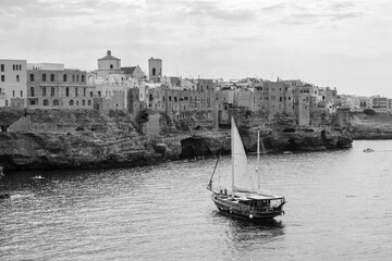 Polignano a Mare skyline from the sea with galeon sail boat, black and white - Bari, Puglia, Italy