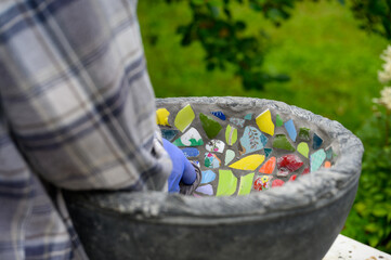 People decorate earthenware with mosaic techniques in the master class or in the fresh air in the workshop. Homemade mosaic flower pot with porcelain pieces.