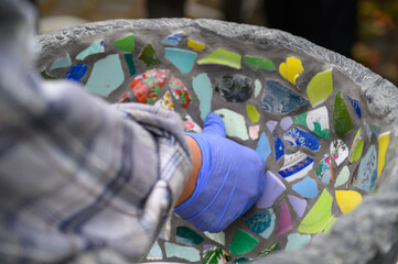 People decorate earthenware with mosaic techniques in the master class or in the fresh air in the workshop. Homemade mosaic flower pot with porcelain pieces.