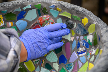 People decorate earthenware with mosaic techniques in the master class or in the fresh air in the workshop. Homemade mosaic flower pot with porcelain pieces.