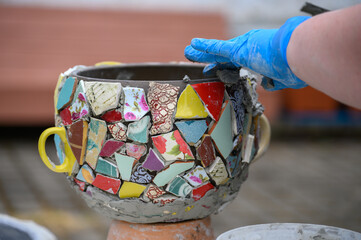 People decorate earthenware with mosaic techniques in the master class or in the fresh air in the workshop. Homemade mosaic flower pot with porcelain pieces.