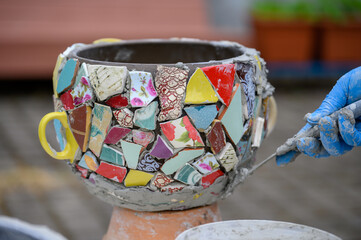 People decorate earthenware with mosaic techniques in the master class or in the fresh air in the workshop. Homemade mosaic flower pot with porcelain pieces.