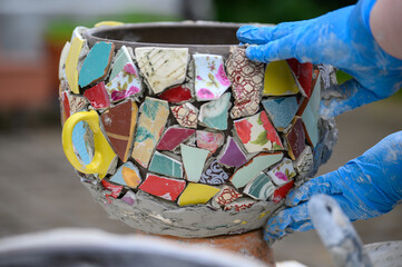 People decorate earthenware with mosaic techniques in the master class or in the fresh air in the workshop. Homemade mosaic flower pot with porcelain pieces.