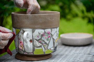 People decorate earthenware with mosaic techniques in the master class or in the fresh air in the workshop. Homemade mosaic flower pot with porcelain pieces.