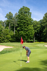 Male golfer putting, golf ball next to the hole with red flag, putt, golf game, green, bunker, trees