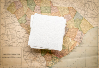 small, blank, square sheet of rough handmade paper floating over vintage defocused map of South...