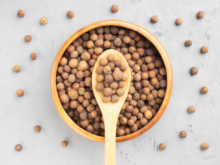 Spice Allspice (Jamaica pepper, Pimento) in wooden bowl and spoon, scattered on gray concrete background. Top view. Indian cuisine concept