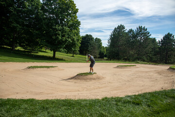 Male golfer in gray with ball in sand trap, bunker shot, end in sight, overcoming obstacles, challenging shot, target in sight, island in bunker