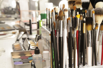 Fototapeta premium Sets of makeup brushes and cosmetics on a bright workplace of a make-up artist. Brushes for applying eye shadow and foundation. Concept: makeup cabinet, stylist and makeup artist tools
