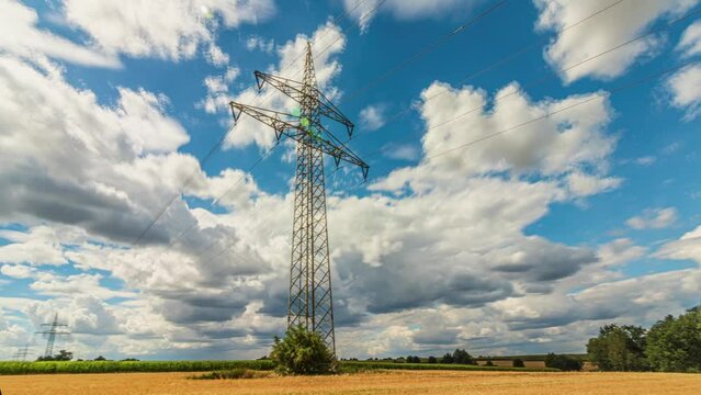 Daytime time lapse panorama of power pylons in the fields outside the city against the backdrop of clouds floating across the blue sky. Expensive electricity. Delivery of electricity. Pan shot