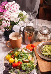 Country breakfast still life with bread, kitchen garden vegetables, herbs and edible flowers, coffee and milk.