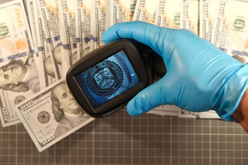 Checking the authenticity of dollars with a currency detector close-up, forensic examination of...