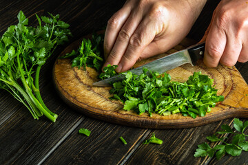 Professional chef cuts green parsley on a cutting board with a knife for preparing a vegetarian dish. Peasant food