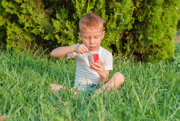 The child eats ice cream in nature. A five-year-old red-haired boy sits in a park on the grass and eats ice cream.