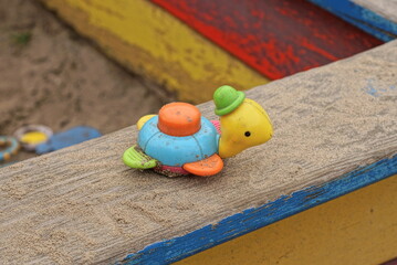 one plastic colored small dirty toy turtle lies on a gray wooden table board outdoors