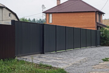 one big closed metal black gate and part of a long iron fence wall on a rural street