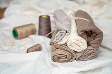 Rolls of linen color fabric with spools of thread. Close-up of natural cotton fabric