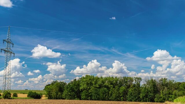 Daytime time lapse panorama of power pylons in the fields outside the city against the backdrop of clouds floating across the blue sky. Expensive electricity. Delivery of electricity. Pan shot