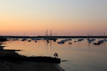 Sunset over Holyhead Marina, Anglesey, Wales while a lone angler finishes for the day.
