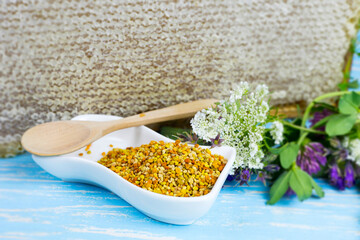 raw organic bee pollen on a wooden board surrounded by wildflowers