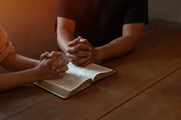 Two people are praying together over holy bible on wooden table
