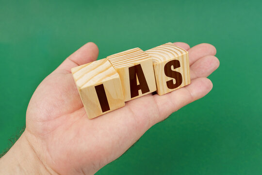 On a green background, in the hands of a person, cubes with the inscription - IAS