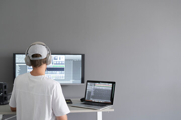 male producer in headphones doing music at home using computer