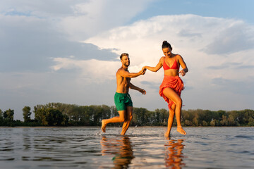 Happy lovely couple running on river beach near the city at sunset. They relaxing after work day.