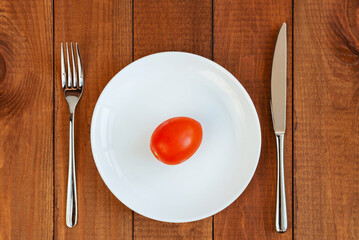Red tomato on a white plate. A plate with vegetables on the table. Diet food. Vegetarian food.
