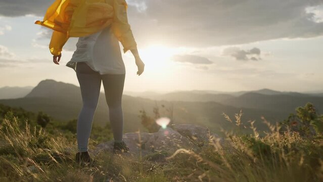 A girl in a yellow jacket climbs the top of the mountain. Woman hiking in the mountains at sunset in a beautiful landscape, freedom and joy. High quality 4k footage
