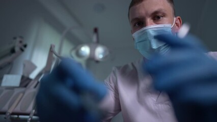 Portrait of focused concentrated dentist using tools treating patient in slow motion. Professional Caucasian young man in uniform examining oral cavity in hospital indoors. Health and medicine concept