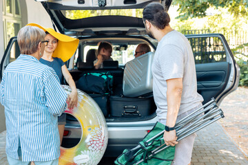 People loading luggage and beach chair in trunk of automobile before leaving on summer holiday vacation at seaside. Big european family travelling with bags on road trip, adventure journey.