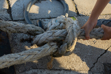 detail of a person pulling a rope or rope with sailor's knots to moor the ship in the harbor on a metal bollard