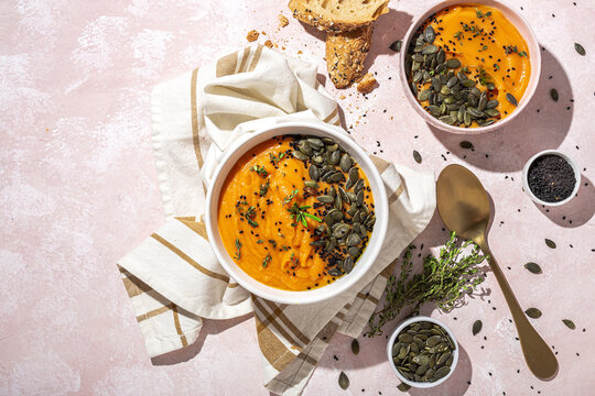 Bowls of healthy pumpkin cream soup served on table near bread slices