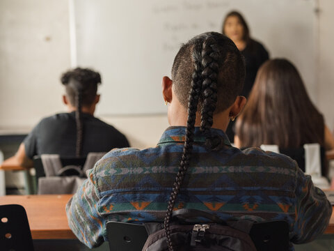Native boy leans head to the right while writing notes in class