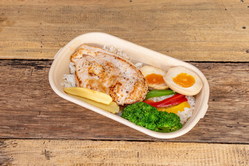 Lunch tray with a combo of boiled egg, white rice, broccoli and other vegetables and a grilled...