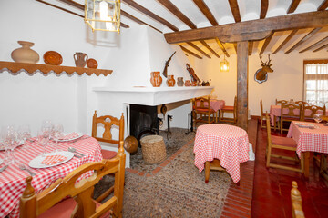 Dining room of a rustic-style village restaurant with a large fireplace with hearth, wooden beams and columns and vintage rustic decorative details
