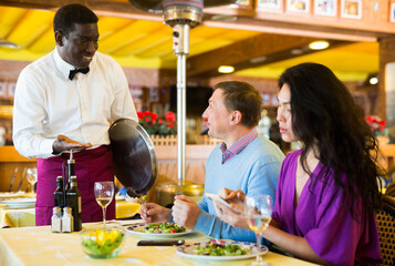 European man and Asian woman talking with African-american man waiter in restaurant.