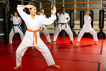 Asian woman in kimono standing in fight stance during group karate training. © JackF