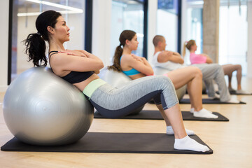 Fototapeta premium Group of adult sports people engaged in fitness in the studio perform a back stretching exercise with a fitball during ..training