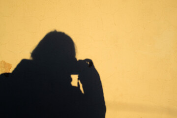 Selfie of a female photographer in the form of a human shadow with a camera on a yellow old shabby wall background. Copy space